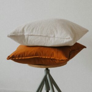 Washed Linen Decorative Pillow stacked on a stool in Warm White and Copper